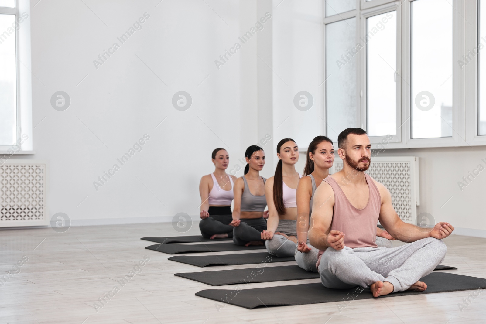 Photo of Group of people meditating on mats in yoga class. Space for text