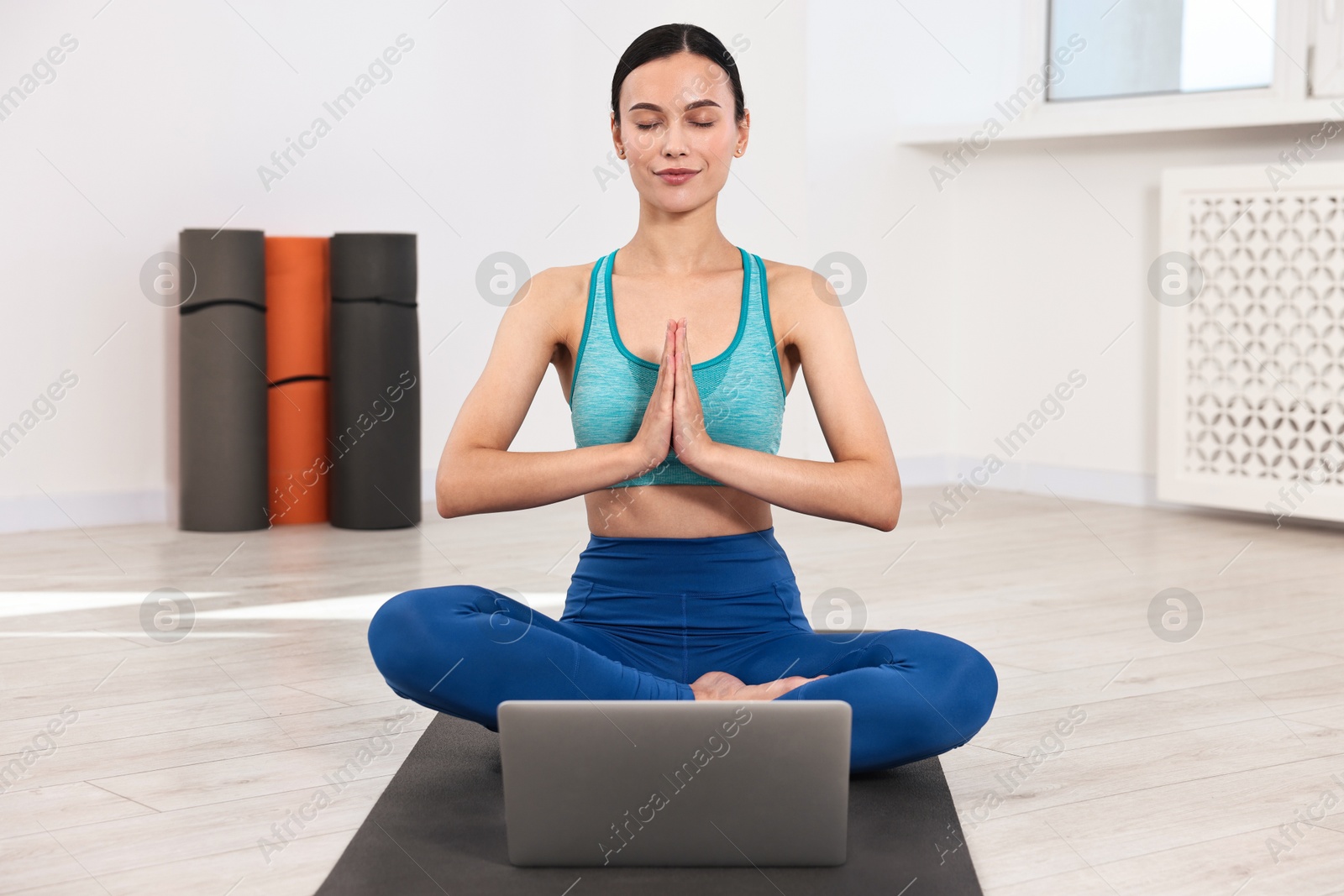 Photo of Woman meditating near laptop on yoga mat at home