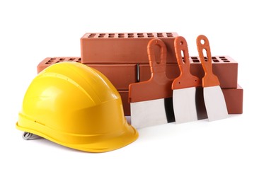 Photo of Yellow hard hat, red bricks and putty knives isolated on white. Building material and construction tools