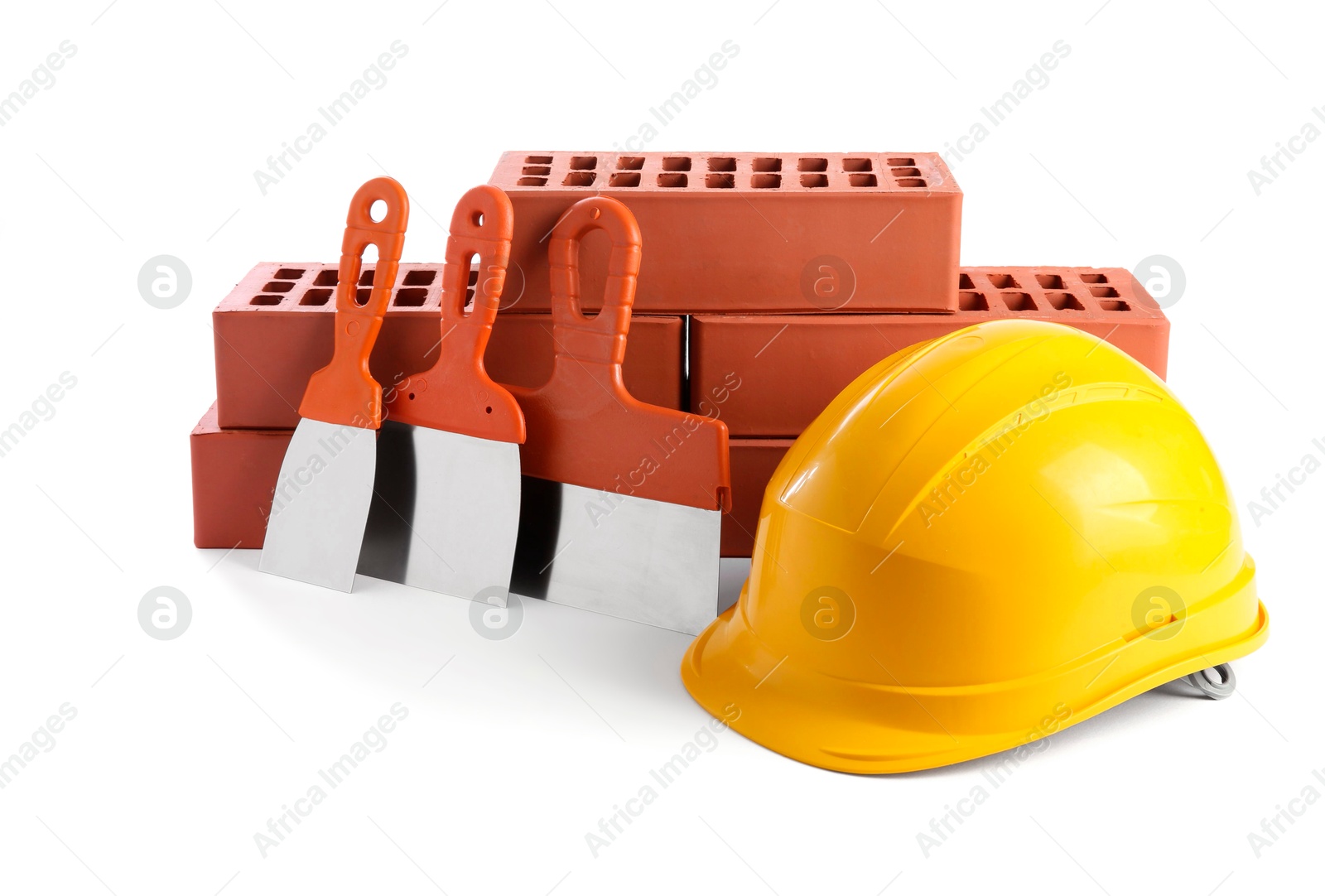 Photo of Yellow hard hat, red bricks and putty knives isolated on white. Building material and construction tools