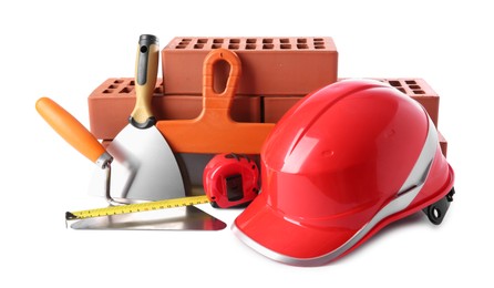 Photo of Orange hard hat, red bricks, trowel, measuring tape and putty knives isolated on white. Building material and construction tools