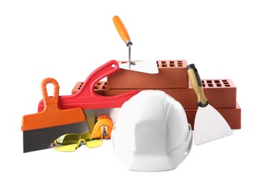 Hard hat, red bricks, trowel, measuring tape, goggles and putty knives isolated on white. Building material and construction tools