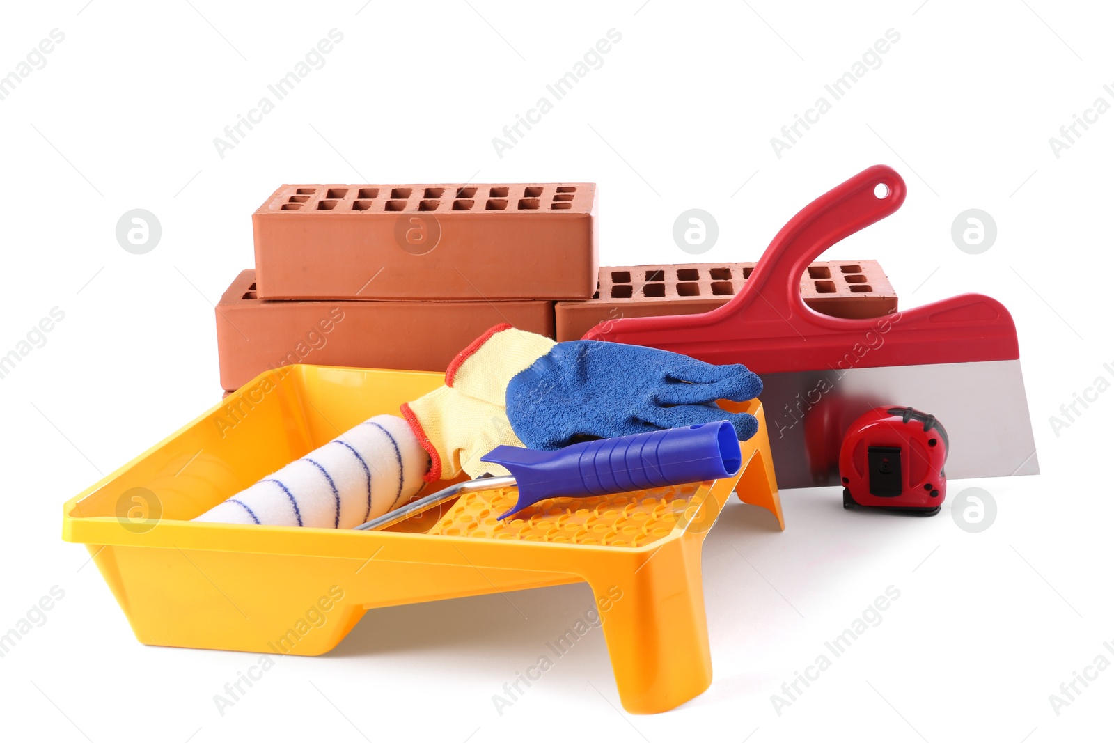 Photo of Red bricks, roller, putty knife, gloves, measuring tape and tray isolated on white. Building material and construction tools