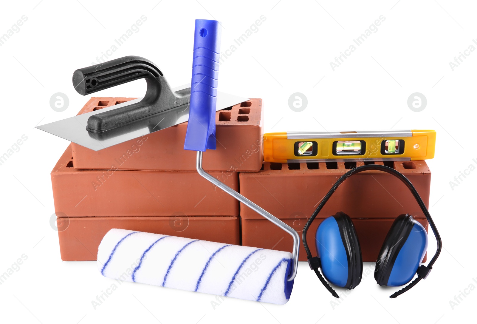 Photo of Red bricks, building level, putty knife, roller and earmuffs isolated on white. Construction tools