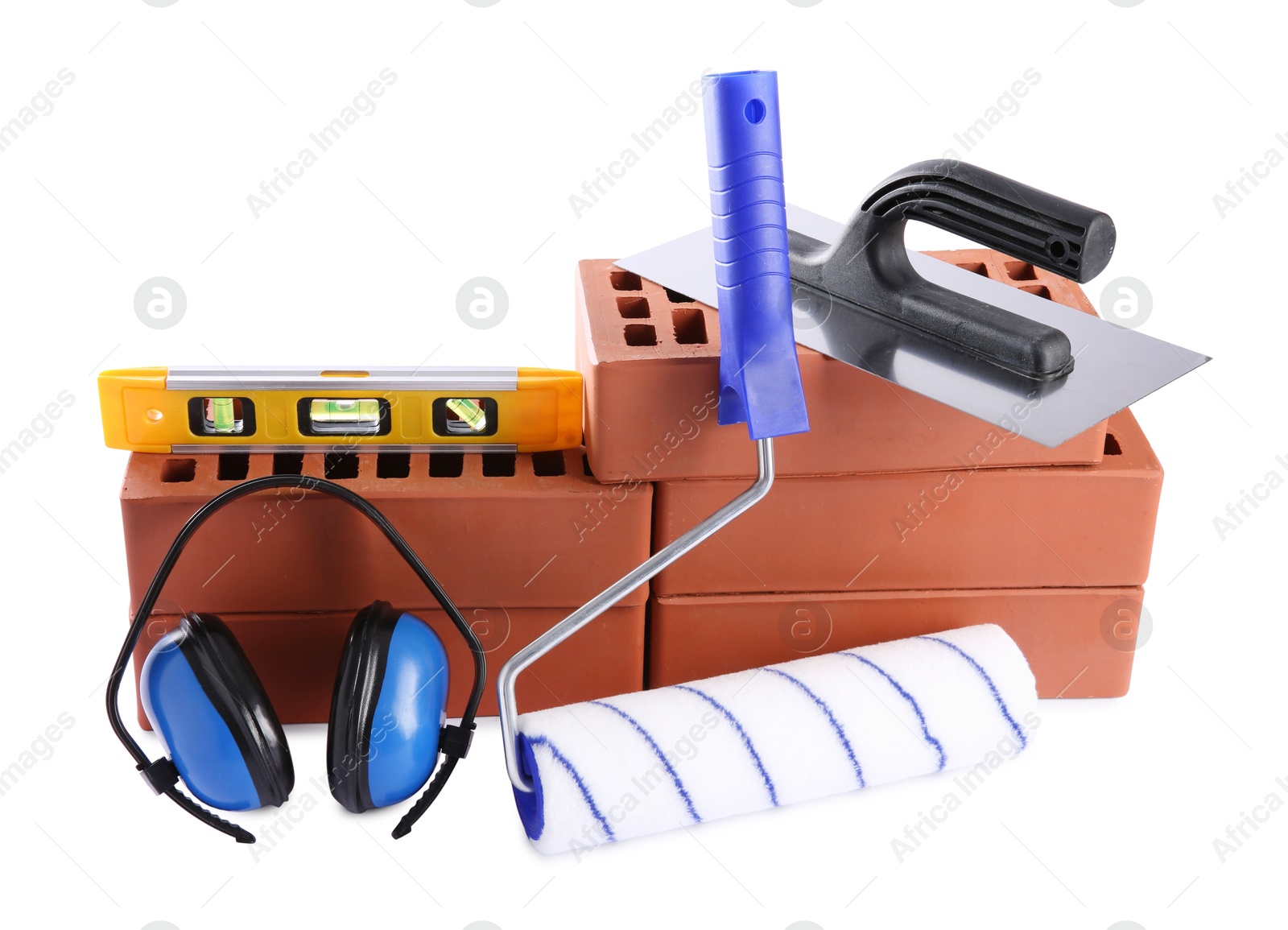 Photo of Red bricks, building level, putty knife, roller and earmuffs isolated on white. Construction tools