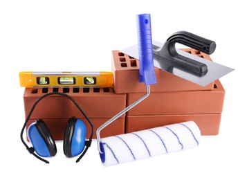 Red bricks, building level, putty knife, roller and earmuffs isolated on white. Construction tools