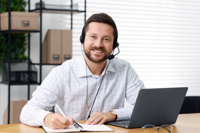 Photo of Interpreter in headset taking notes while having video chat via laptop at wooden table indoors