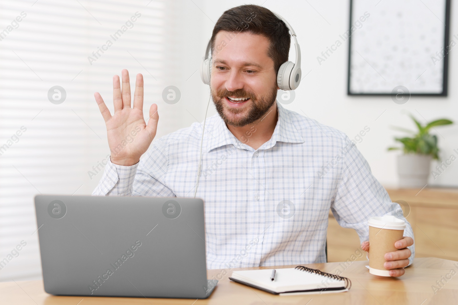 Photo of Interpreter in headphones having video chat via laptop at wooden table indoors