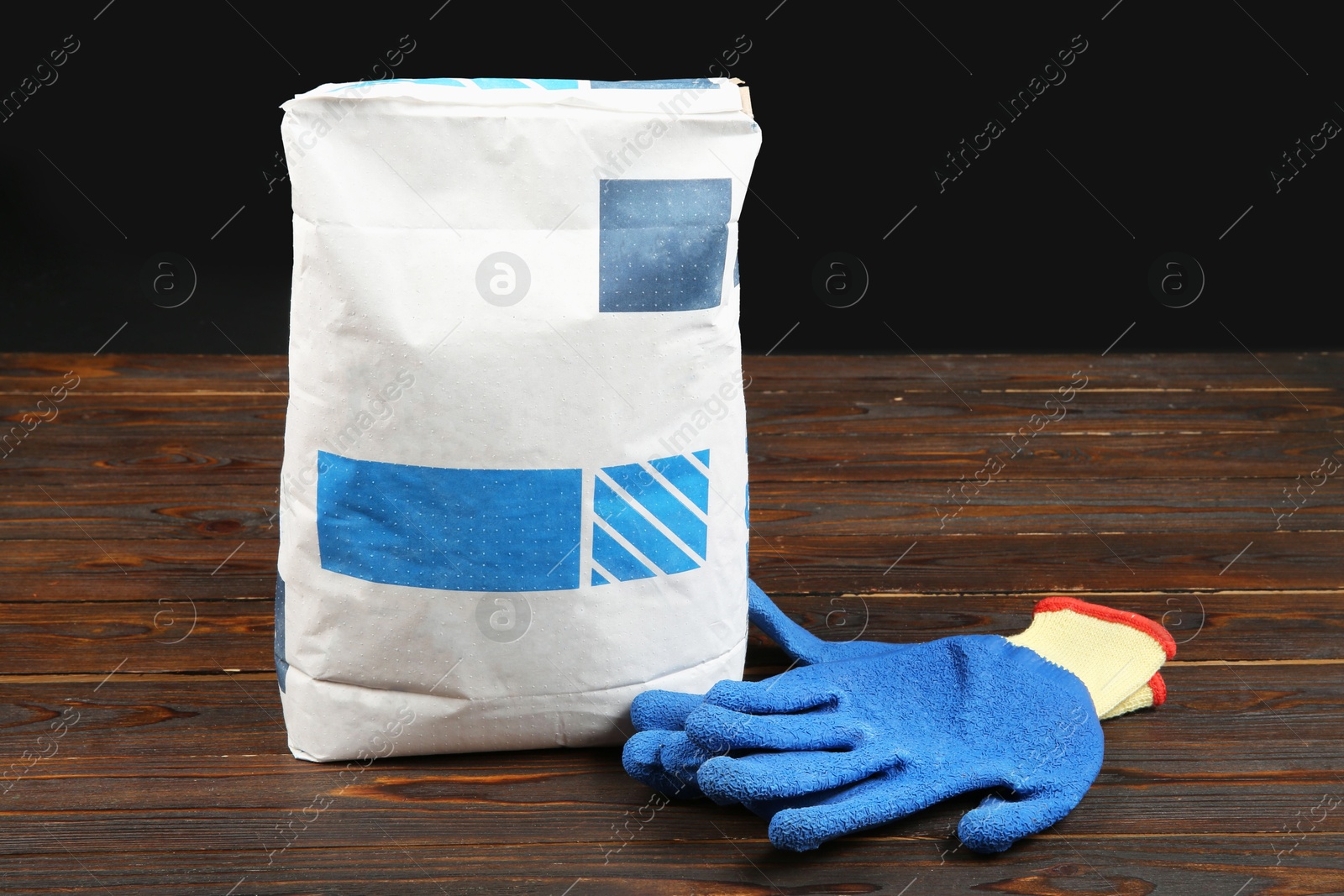 Photo of Bag of cement powder and rubber gloves on wooden table. Building material