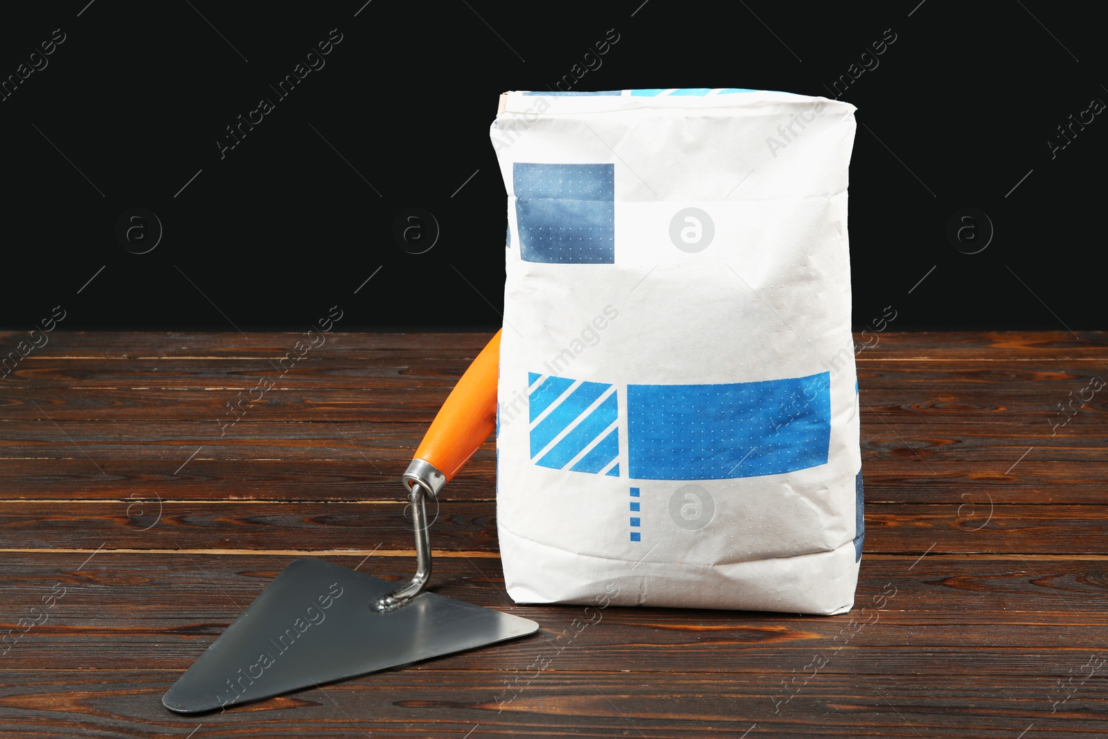 Photo of Bag of cement powder and putty knife on wooden table. Building material