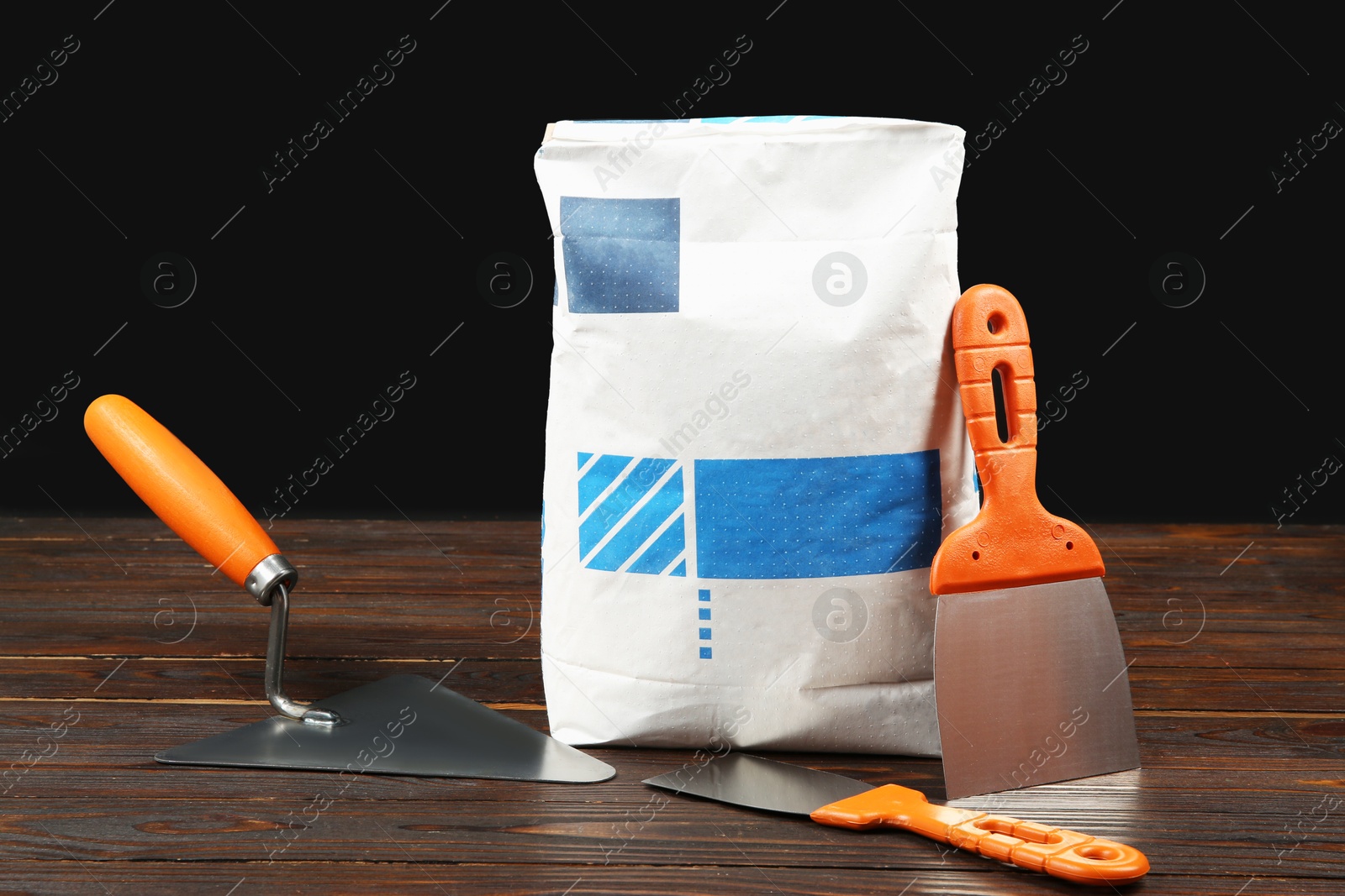 Photo of Bag of cement powder and putty knives on wooden table. Building material