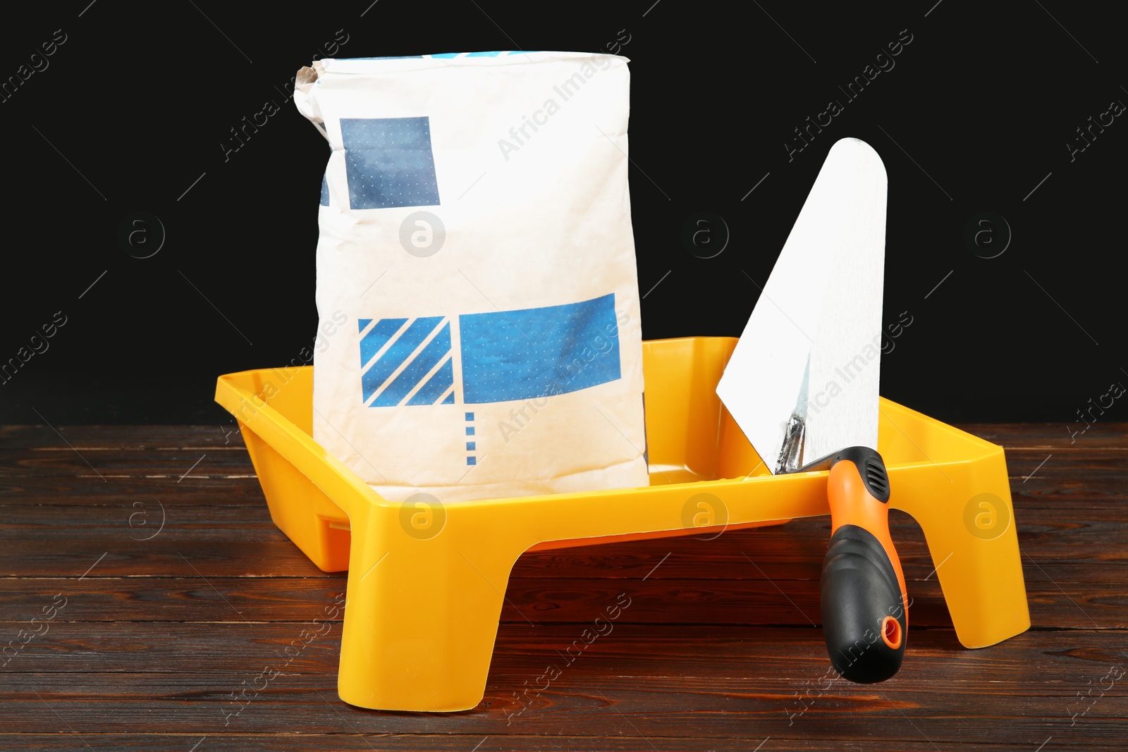 Photo of Bag of cement powder, tray and putty knife on wooden table. Building material and construction tools