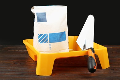 Bag of cement powder, tray and putty knife on wooden table. Building material and construction tools