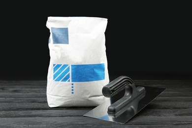 Photo of Bag of cement powder and putty knife on dark wooden table. Building material