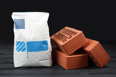 Red bricks and bag of cement powder on dark wooden table. Building materials