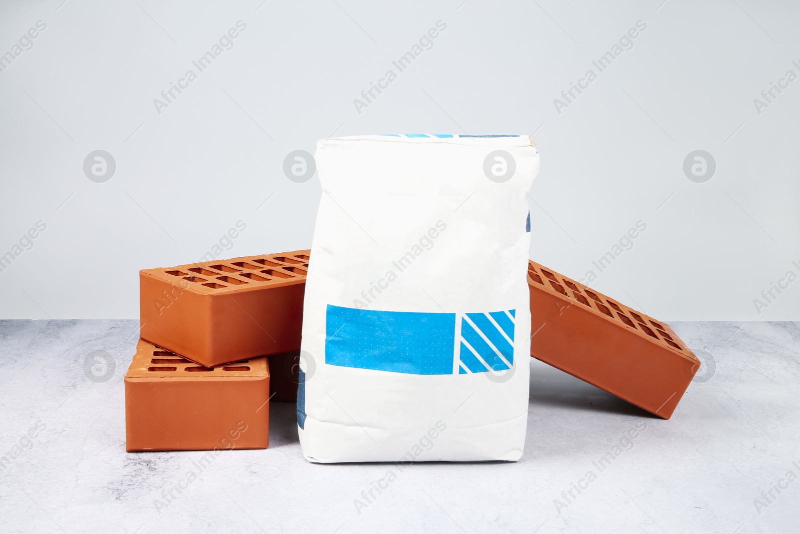 Photo of Red bricks and bag of cement on textured table against light background. Building material