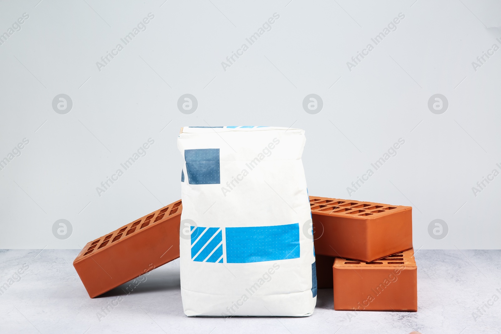 Photo of Red bricks and bag of cement on textured table against light background. Building material