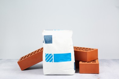 Red bricks and bag of cement on textured table against light background. Building material