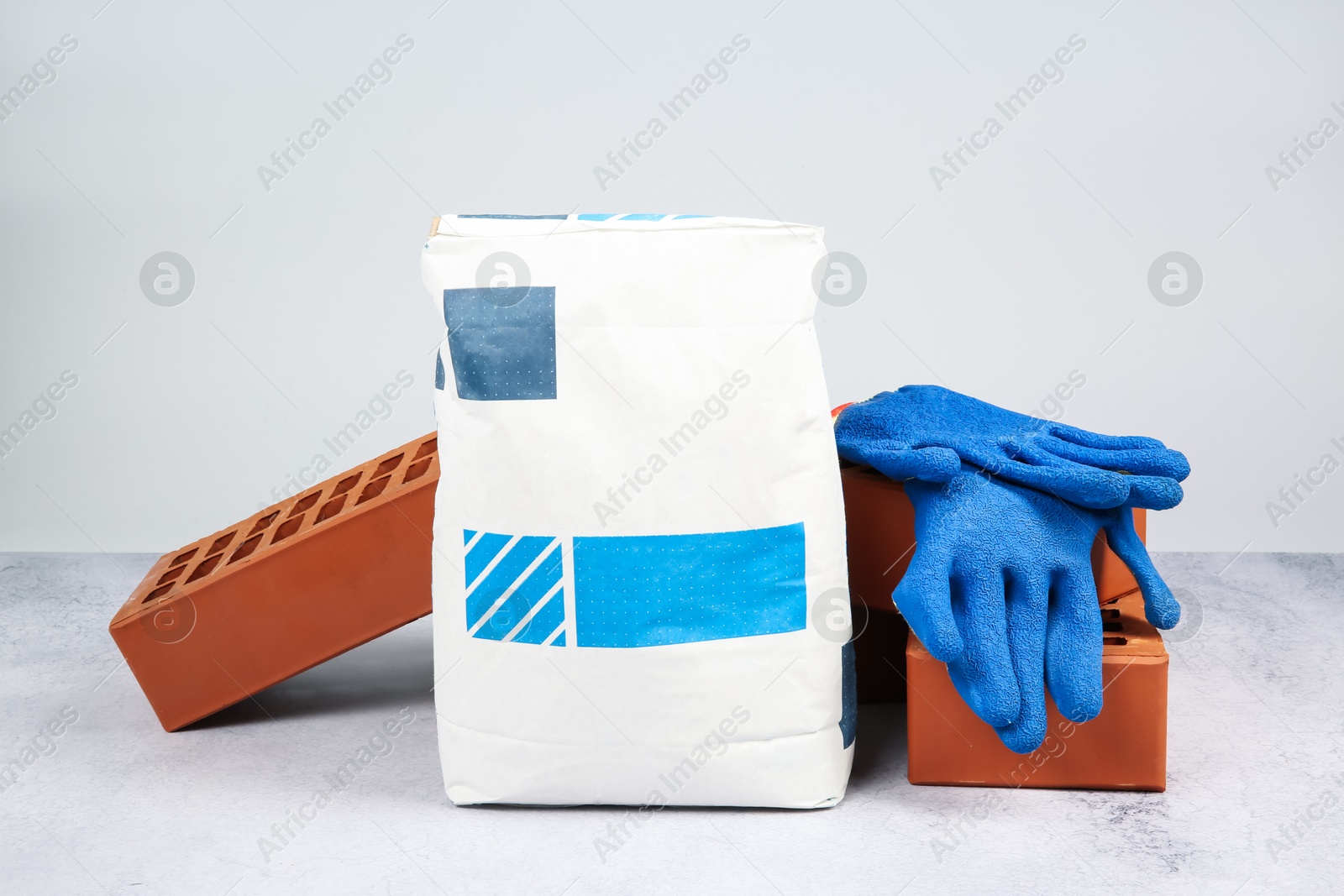 Photo of Red bricks, bag of cement and gloves on textured table against light background. Building material