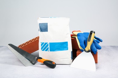 Photo of Red bricks, bag of cement, trowels and gloves on textured table against light background