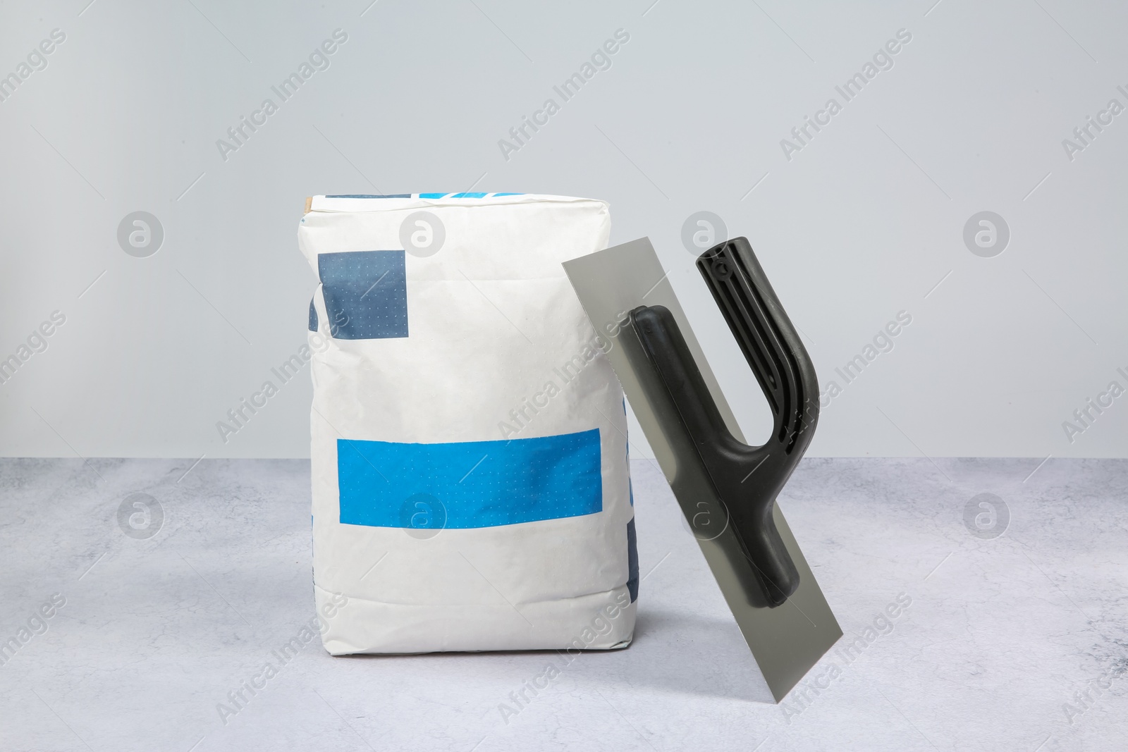 Photo of Bag of cement and plastering trowel on textured table against light background. Building material