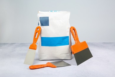 Photo of Bag of cement and trowels on textured table against light background. Building material