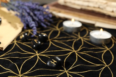 Photo of Black runes and burning candles on divination mat, closeup