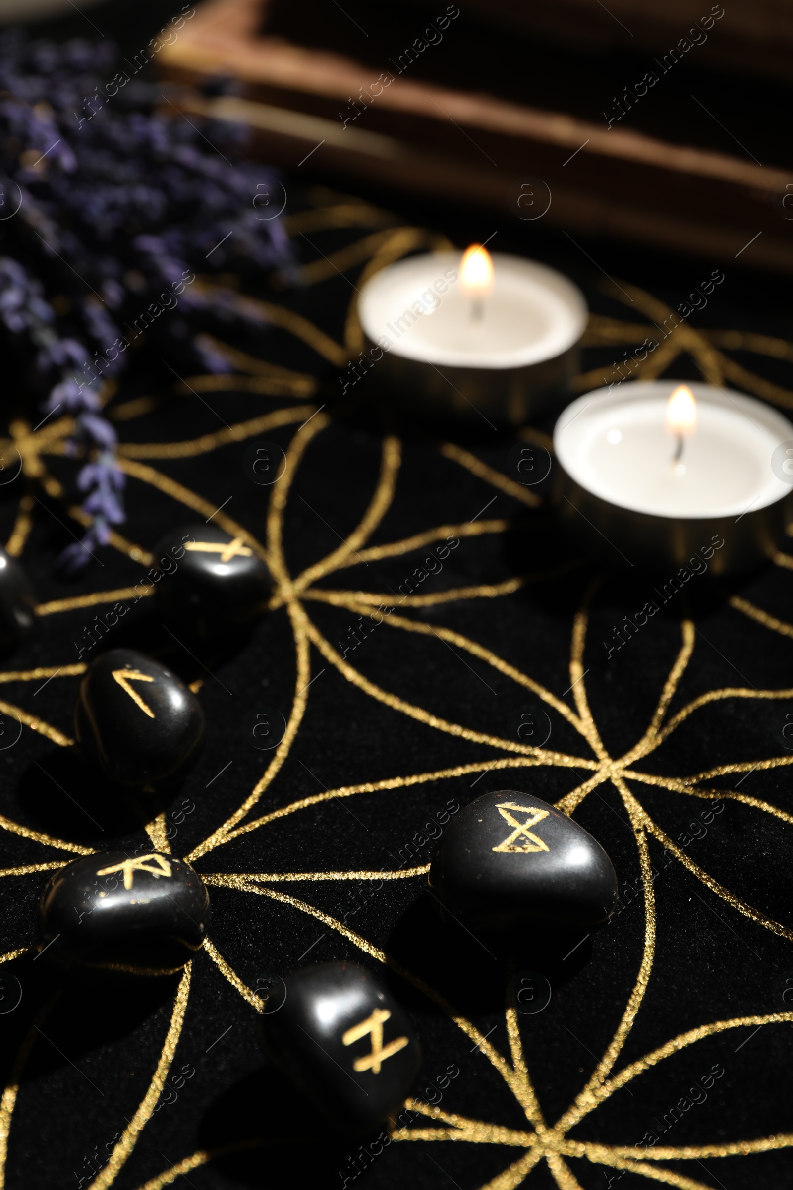 Photo of Black runes and burning candles on divination mat, closeup