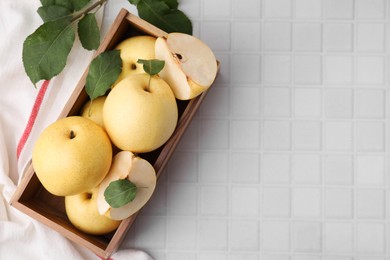 Photo of Delicious fresh apple pears in wooden crate and leaves on white tiled table, top view. Space for text