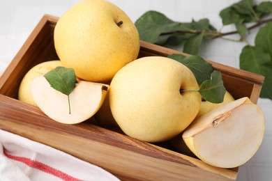 Photo of Delicious fresh apple pears in wooden crate and green leaves on table, closeup