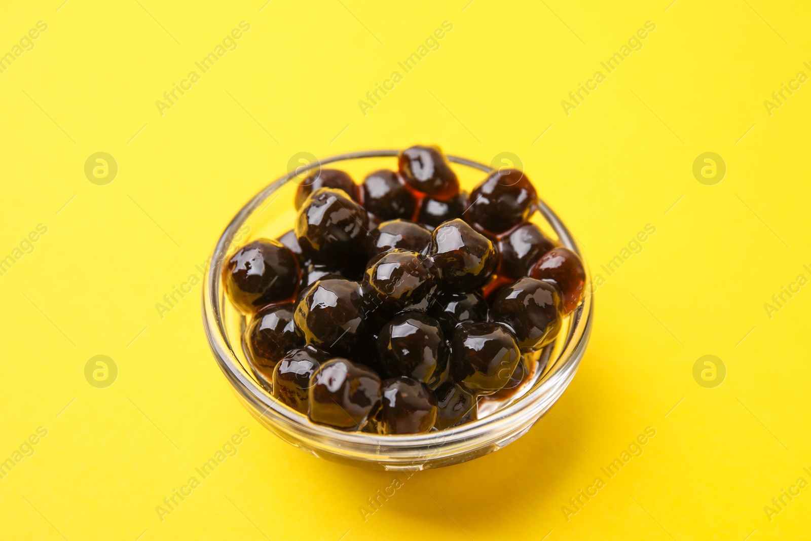 Photo of Dark tapioca pearls in bowl on yellow background, closeup