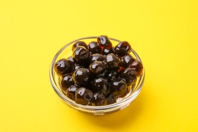 Photo of Dark tapioca pearls in bowl on yellow background, closeup