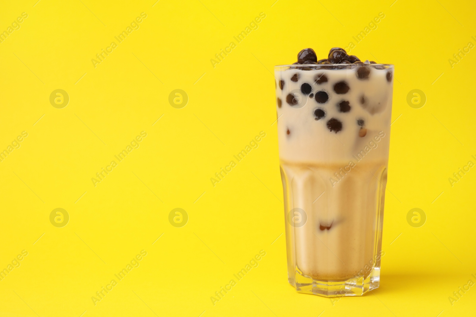 Photo of Tasty milk bubble tea in glass on yellow background, space for text