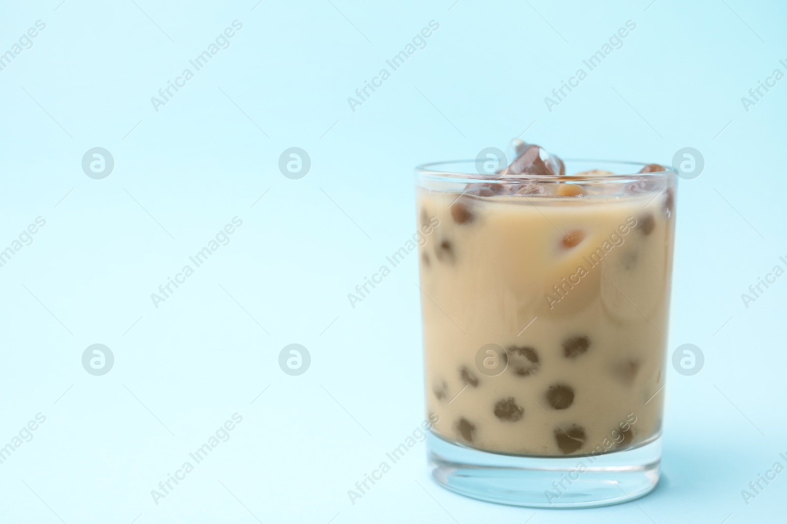 Photo of Tasty milk bubble tea in glass on light blue background, space for text