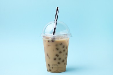 Photo of Tasty milk bubble tea in plastic cup on light blue background