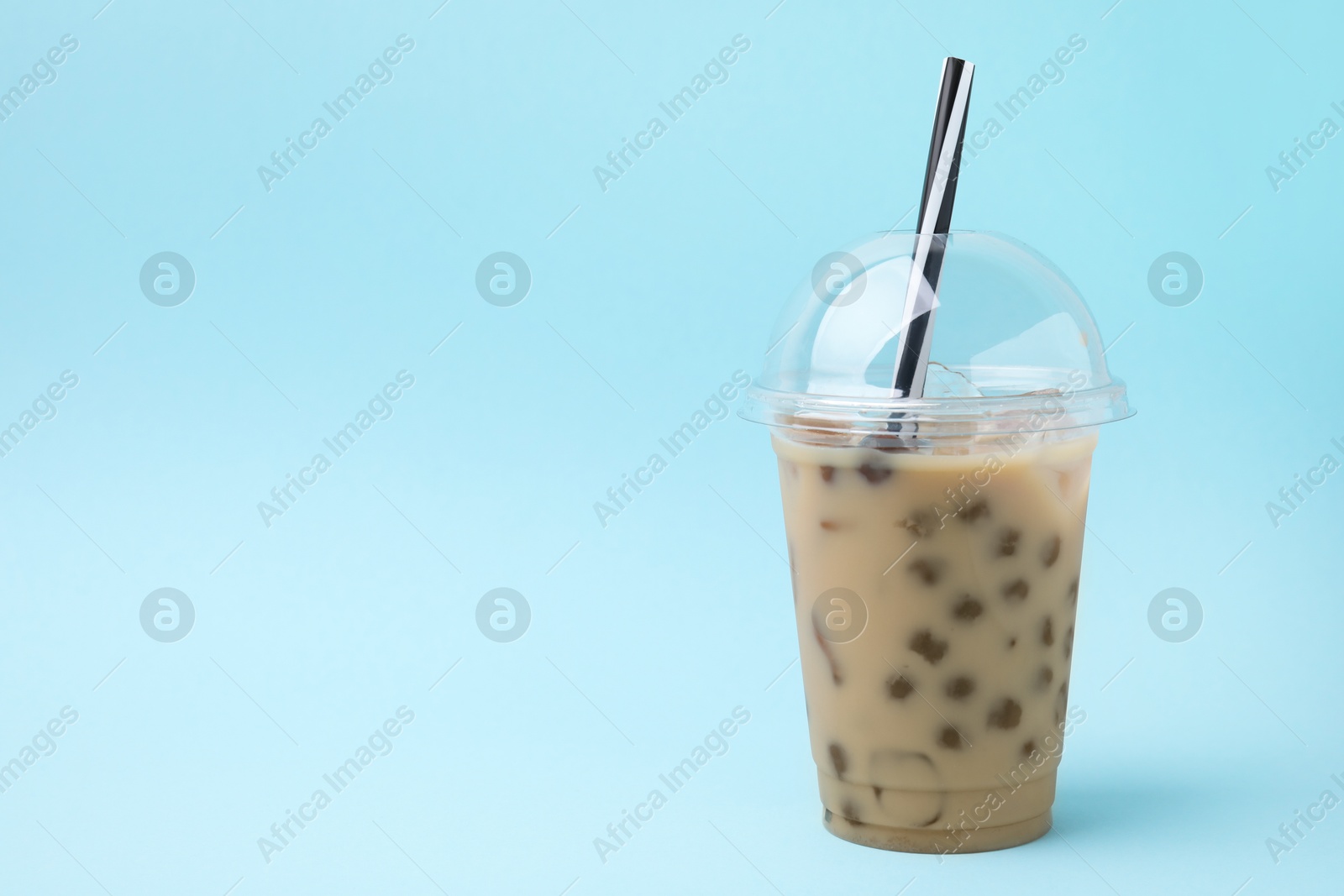 Photo of Tasty milk bubble tea in plastic cup on light blue background, space for text