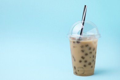 Photo of Tasty milk bubble tea in plastic cup on light blue background, space for text