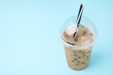 Photo of Tasty milk bubble tea in plastic cup on light blue background, closeup. Space for text