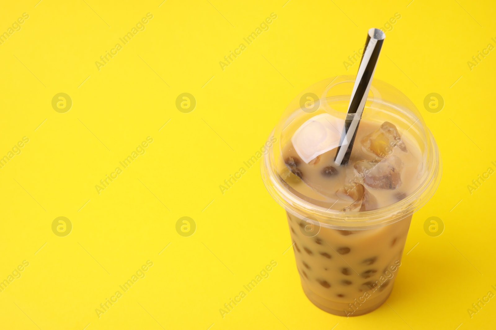 Photo of Tasty milk bubble tea in plastic cups on yellow background, closeup. Space for text