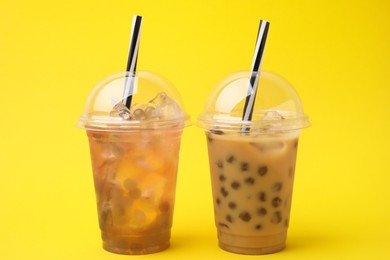 Photo of Tasty bubble tea in plastic cups on yellow background