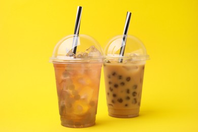 Photo of Tasty bubble tea in plastic cups on yellow background