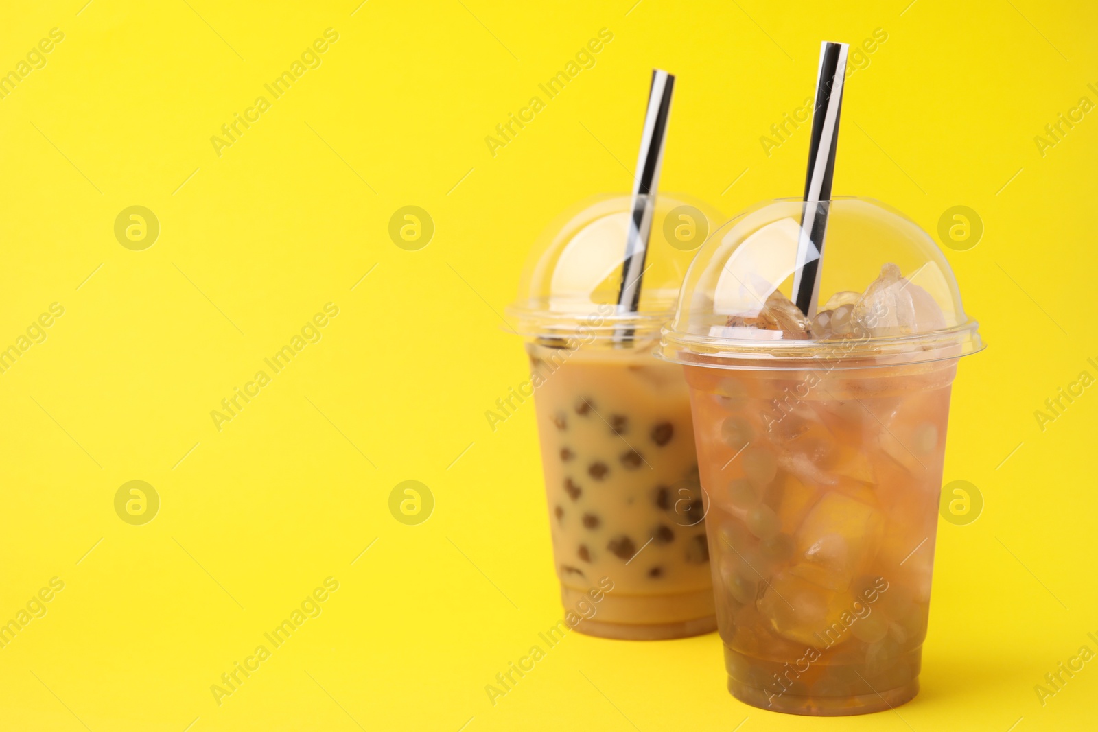 Photo of Tasty bubble tea in plastic cups on yellow background, space for text