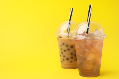 Photo of Tasty bubble tea in plastic cups on yellow background, space for text