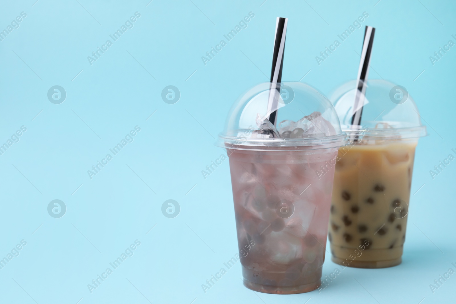 Photo of Tasty bubble tea in plastic cups on light blue background, space for text