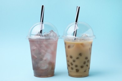 Photo of Tasty bubble tea in plastic cups on light blue background