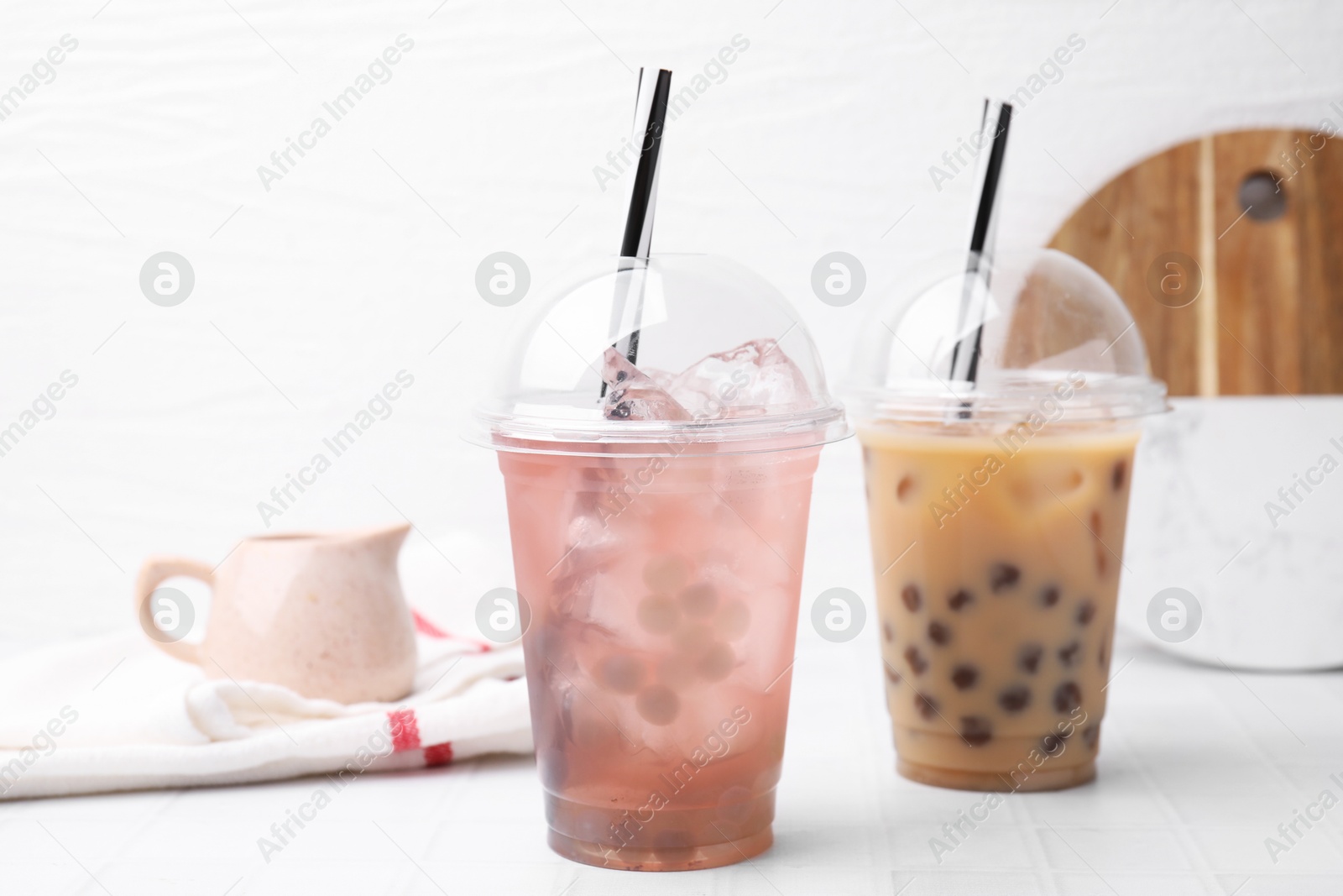 Photo of Tasty bubble tea in plastic cups on white tiled table