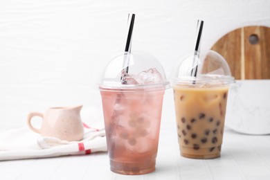 Photo of Tasty bubble tea in plastic cups on white tiled table