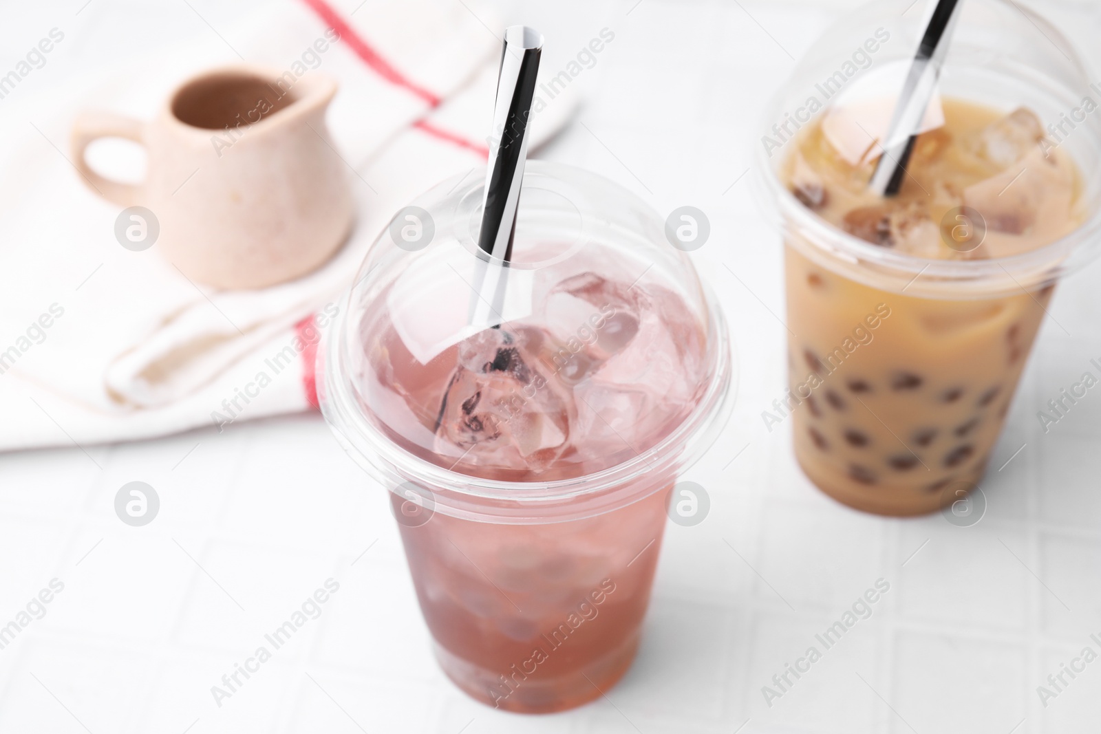 Photo of Tasty bubble tea in plastic cups on white tiled table, closeup