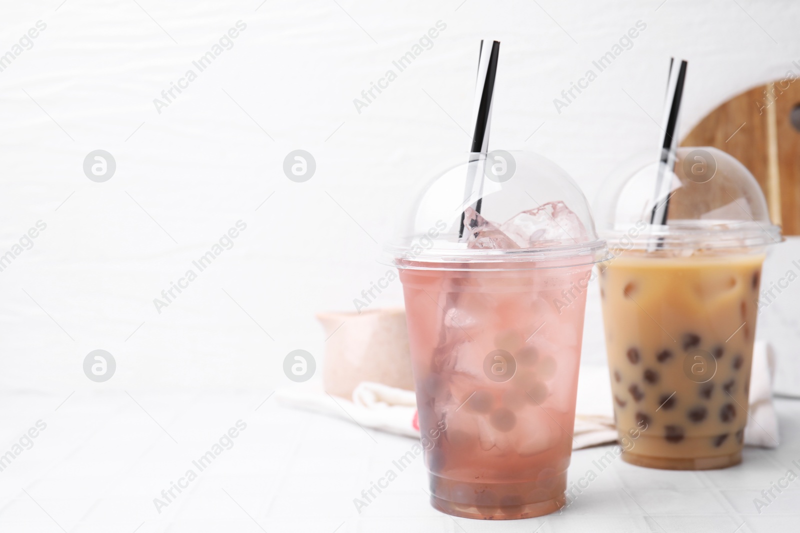 Photo of Tasty bubble tea in plastic cups on white tiled table, space for text