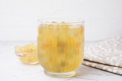 Photo of Tasty bubble tea in glass and tapioca pearls on white table, closeup